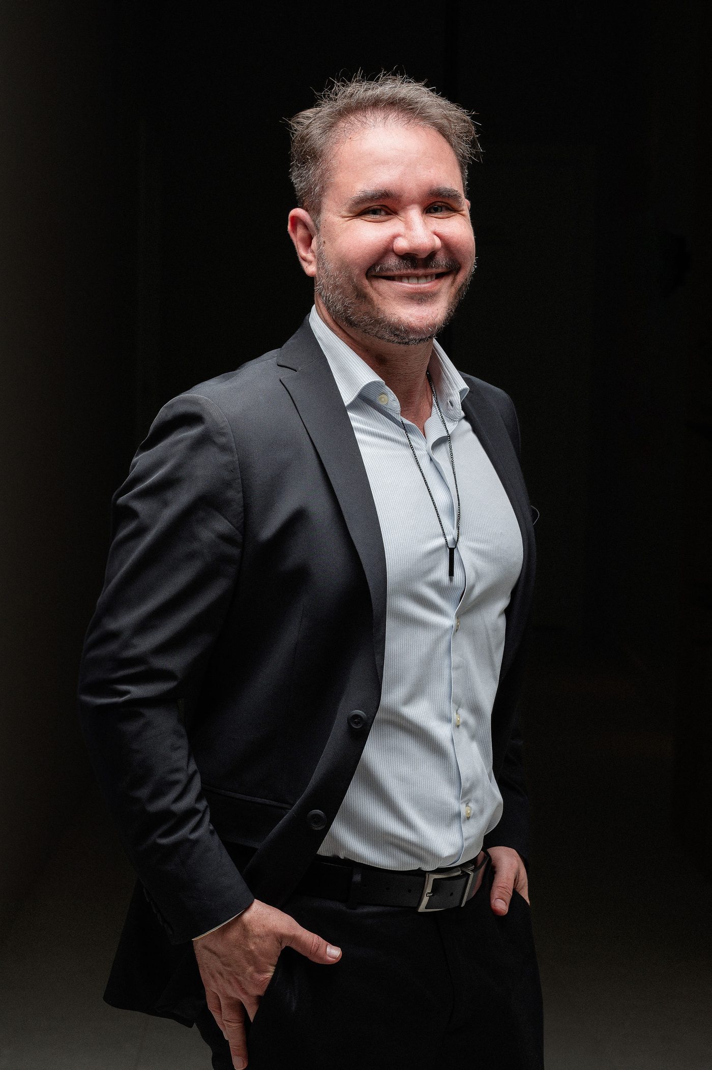 Dr. Marcelo Rebecca, médico, sorrindo de blazer em fundo escuro