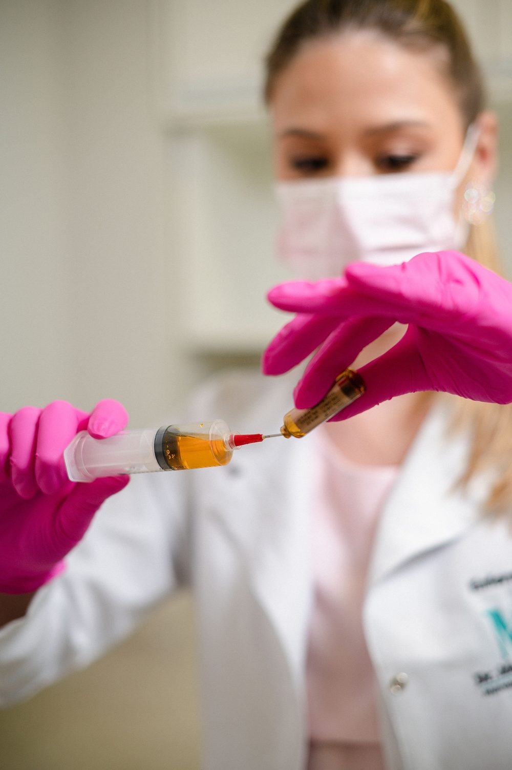 Profissional de saúde de luvas rosa preparando seringa com terapia hormonal