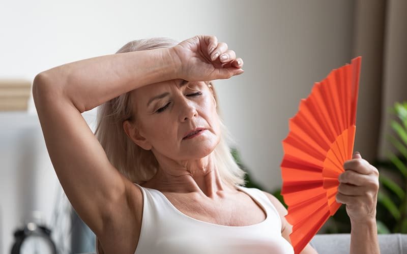 Mulher madura com sensação de calor, abanando o rosto com um leque